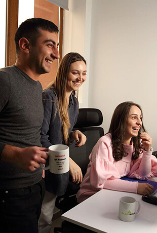 Three employees standing and looking at a computer screen laughing