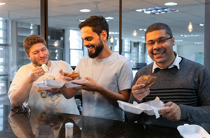 Three men eating donuts and smiling