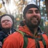 Bearded man wearing an orange jacket with a backpack and a baby